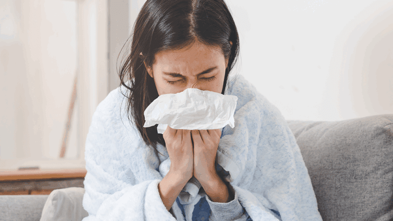 A woman with a cold sneezing into a tissue.