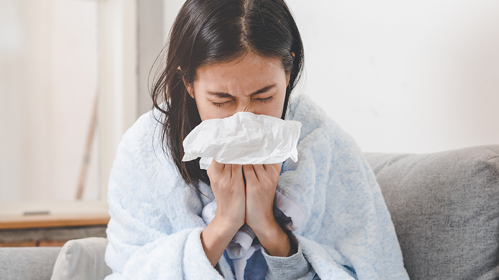 A woman with a cold sneezing into a tissue.