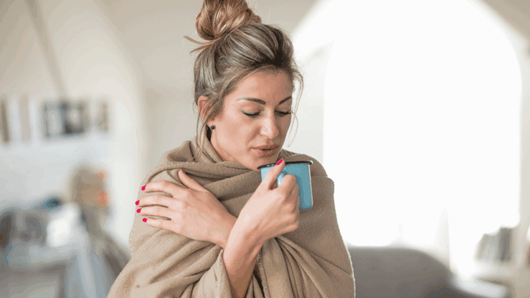 A woman wrapped in a blanket sipping some tea with adaptogens to combat a cold.