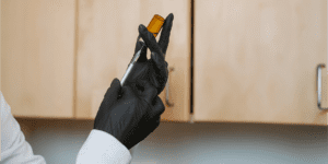 Healthcare provider in black gloves drawing from an amber vial with a syringe, preparing a medically supervised peptide therapy injection.