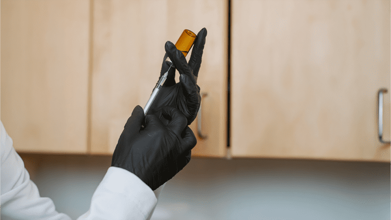 Healthcare provider in black gloves drawing from an amber vial with a syringe, preparing a medically supervised peptide therapy injection.