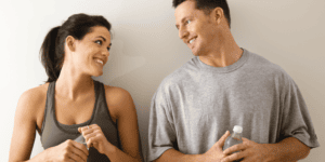 Smiling active man and woman in athletic wear holding water bottles after a workout, illustrating recovery and healthy aging for a post on ipamorelin peptide therapy in Scottsdale.