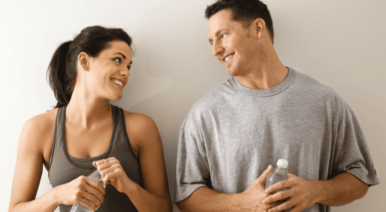 Smiling active man and woman in athletic wear holding water bottles after a workout, illustrating recovery and healthy aging for a post on ipamorelin peptide therapy in Scottsdale.